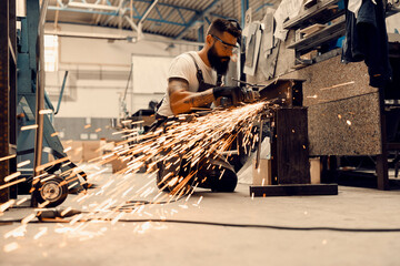 Wall Mural - A metal industry worker processing metal parts with grinder at workshop.