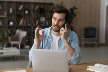Wall Mural - telephone call and computer work. young male employee working at home office take break in using lap