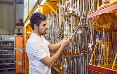 Wall Mural - Young man shopping at a DIY store. Serious male customer standing in the hose aisle and trying to choose a new good quality stainless steel hose. Hardware shopping concept