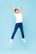 Cheerful Asian mixed race boy jumping and raising hands up in isolated light blue color studio background