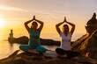 © unai - Two women sitting on yoga mat in nature by the sea at sunset, healthy and naturist life, outdoor pilates, virasana