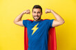 Young handsome caucasian man isolated on yellow background in superhero costume and doing strong gesture