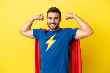 Young handsome caucasian man isolated on yellow background in superhero costume and doing strong gesture