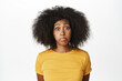 © Cookie Studio - Close up portrait of funny african american lady pouting, making silly clueless face, standing in yellow t-shirt against white background