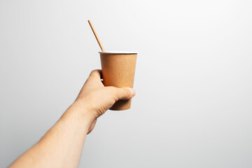 Close-up of male hand holding paper cup of coffee with bamboo straw on white.