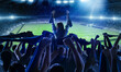Back view of football, soccer fans cheering their team with scarfs at crowded stadium at evening time. Concept of sport, support, competition. Out of focus effect
