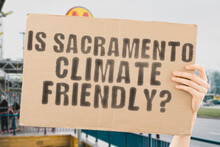 The Question " Is Sacramento Climate-friendly? " Is On A Banner In Men's Hands With Blurred Background. Support. Team. Activist. Urban. Sunset. Carbon. Ecology. Energy. New. Clean. Warming. Waste