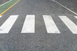White road crosswalk or crossing path on asphalt road. The pedestrian control path is painted green beside of the road.