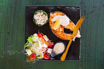 salmon fish steak grill lemon with nut in spinach and vegetable fruits salad with sauce and tomato on black dish with gold or brass knife for seafood and omega 3 in restaurant on top view green table