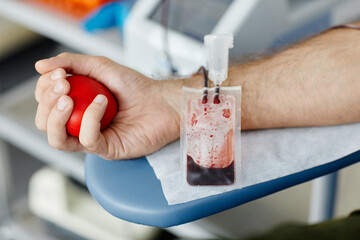 Poster - Close up of male hand squeezing stress ball while donating blood at medical volunteer center focus on blood bag in foreground, copy space