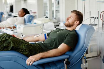 Wall Mural - Side view portrait of military man donating blood while laying in chair at plasma donation center