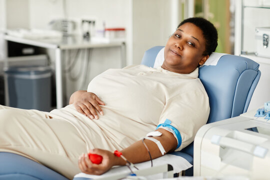 portrait of smiling woman giving blood while laying in chair at blood donation center and looking at