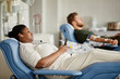 © Seventyfour - Side view portrait of two people giving blood and lying in chairs at donation center, copy space