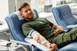 canvas print picture - Portrait of smiling young man giving blood at donor center in comfort while lying in chair, copy space