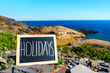 Wall Mural - Black board with word holidays against sea coast