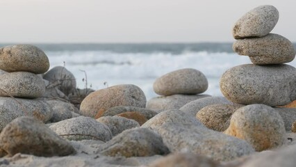 Wall Mural - Rock balance on pebble beach, Monterey 17-mile drive, California coast, USA. Stable pyramid stacks of round stones, sea ocean water waves crashing at sunset. Zen meditation Seamless looped cinemagraph