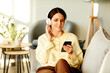 © Seventyfour - Modern young adult Caucasian woman wearing stylish casual clothes relaxing on sofa in living room at home listening to music in wireless headphones