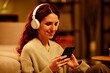 © Seventyfour - Medium close-up portrait of joyful young adult Caucasian woman with long curly hair spending evening at home listening to music and surfing Internet on s,artphone