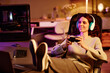 © Seventyfour - Modern young adult Caucasian woman wearing casual clothes and headphones spending evening playing video games with use of controller