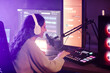 © Seventyfour - Young woman with long curly hair wearing headphones working in amateur radio station telling stories and turning on music for listeners