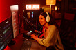 © Seventyfour - Joyful young adult Caucasian woman with long curly hair wearing casual outfit and headphones telling stories to listeners during radio broadcasting at night
