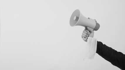 Wall Mural - Megaphone and face mask in Male Hand and he wear black shirt on white background. Black and white ,Studio shooting.