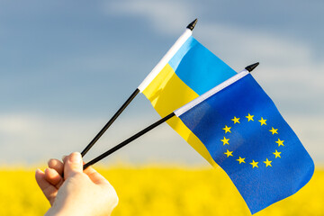 Flags of Ukraine and the European Union held in a woman's hand against the background of the sky and blooming fields, Concept of political cooperation and the hope of Ukrainians for joining the Union