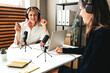 Two happy women host streaming audio podcast using microphone and laptop at home broadcast studio