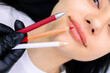 master of permanent makeup in a black glove holds marking pencils in front of the model's lips