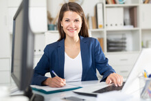 Portrait Of Confident Smiling Female Office Employee During Daily Work With Laptop And Documents