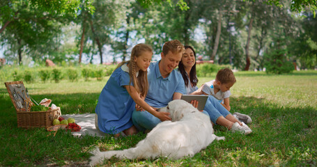 happy family use tablet on picnic. parents watching laptop with two kids outside