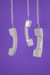 Three handsets hanging on wires on a purple background. Minimal concept.