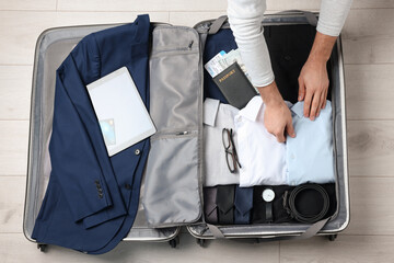 Poster - Man packing suitcase for business trip on wooden floor, top view