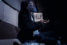 A Homeless Bearded Man Sits On Boxes On The Street And Asks For Help. Need A Homeless Person Asks For Money For Food And Overnight.