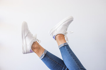 Female feet in sneakers raised up. Isolated on white background.
