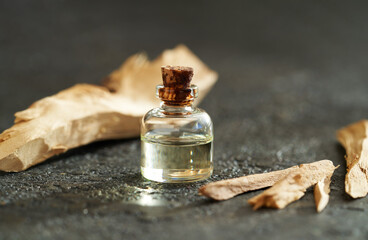 Wall Mural - A bottle of sandalwood essential oil with white sandalwood on dark background