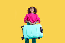 Happy Child Going On Summer Vacation. Black Kid With Suitcase Standing Isolated On Yellow Background. Beautiful African American Girl In Trendy Casual Outfit Carrying Her Heavy Turquoise Travel Bag