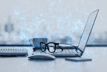 Close Up Of Office Desktop With Supplies, Glasses, Coffee Cup, Laptop And Blue Polygonal Mesh On Blurry City View Background. Technology, Security And Web Hacking Concept. Double Exposure.