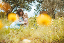 Mother Embracing Daughter Sitting In Meadow