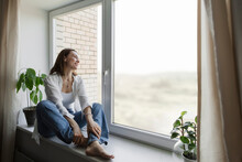 Happy Mature Woman Sitting On Window Sill At Home