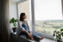 Mature Woman Sitting On Window Sill At Home