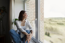 Smiling Mature Woman Sitting On Window Sill At Home