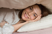 Happy Mature Woman With Teddy Bear Toy Lying Under Blanket On Bed At Home