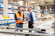 © Westend61 - Worker discussing over tablet PC with manager standing by conveyor belt in warehouse