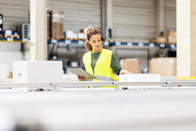 Young Worker With Tablet PC Examining Box On Conveyor Belt In Warehouse