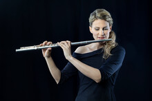 Mature Woman Playing Flute Against Black Background