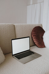 Laptop computer with blank screen on comfortable beige sofa with pillows. Aesthetic influencer styled workspace interior design template with mockup copy space