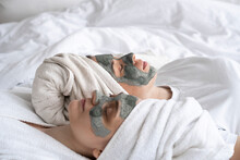 Friends Wearing Facial Masks Lying On Bed At Home