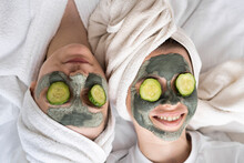 Happy Friends Wearing Facial Masks Relaxing On Bed At Home