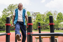 Happy Active Senior Man Exercising On Gymnastics Bar At Park